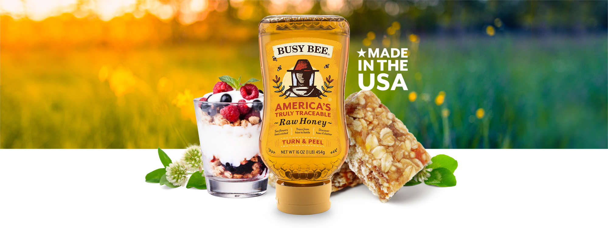 Yogurt parfait, granola bars, and a bottle of Busy Bee Honey in the foreground. Busy Bee Unfiltered Raw Honey Made in the U.S.A. Sunny field in background